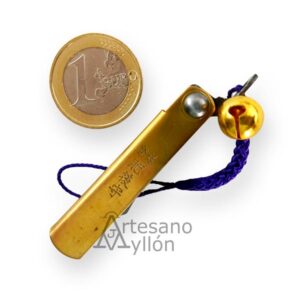 Navaja japonesa Nagao Higonokami cerrada con mango de latón grabado, cordón morado con cascabel dorado y moneda de 1 euro para referencia de tamaño.