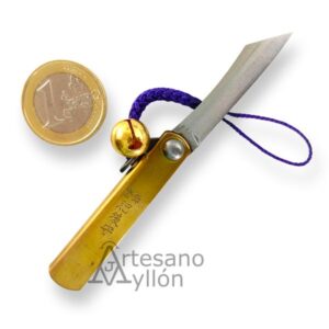 Navaja japonesa Nagao Higonokami abierta con hoja de acero carbono SK de 3,5 cm, mango de latón grabado, cordón morado con cascabel dorado y moneda de 1 euro como referencia de tamaño.