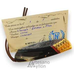 Navaja Miguel Nieto ART3 cerrada, colocada delante del certificado artesanal manuscrito. Se aprecia el mango de cuerno de carnero en tonos oscuros, la virola de latón grabada a mano y parte de la hoja decorada.
