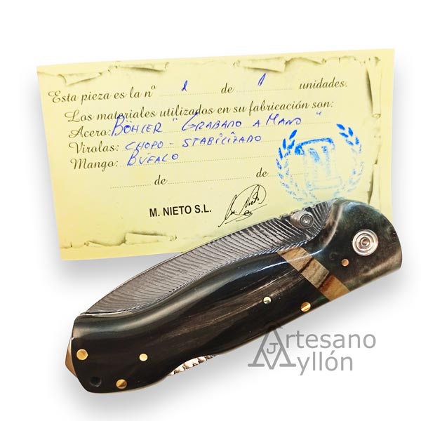 Navaja Miguel Nieto ART4 cerrada, apoyada sobre su certificado artesanal escrito a mano. La hoja grabada es parcialmente visible y se aprecia el mango de búfalo con incrustaciones y la virola decorada.