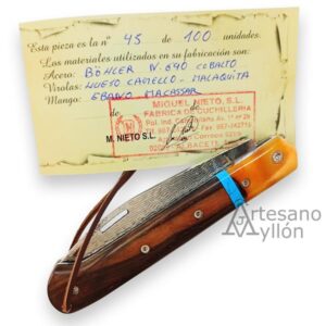 Navaja Miguel Nieto ART5 cerrada vista desde arriba, mostrando el mango de ébano Macassar, la virola de hueso de camello y malaquita azul. Aparece detrás el certificado donde figura el acero Böhler N690, hueso de camello, malaquita y ébano Macassar.