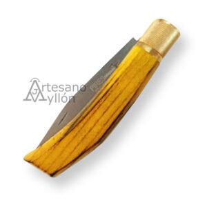 Navaja Pires Agricultor cerrada, vista desde su lateral. Se observa la hoja parcialmente oculta dentro del mango amarillo de madera de fresno, con vetas oscuras. La virola de latón está completamente visible y destaca por su brillo dorado. La forma curva del mango permite apreciar su ergonomía y acabado liso.