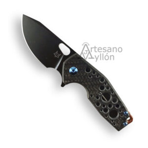 Navaja Fox Suru 526LE TIBSW abierta con hoja de acero Böhler M390 con recubrimiento negro stone washed, filo liso, orificio de apertura, mango de fibra de carbono perforado con tornillos azules y espaciador de cobre, fondo blanco.