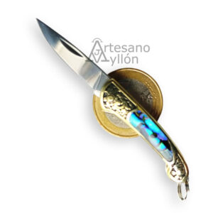 Navaja Third miniatura N89-7 abierta con hoja de acero 420 de 27 mm, mango con virolas de latón dorado e inserción de abulón multicolor, colocada sobre fondo blanco junto a una moneda para mostrar su tamaño real.