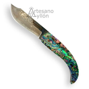 Navaja Tramuntana N91DV abierta con hoja corta de acero de Damasco de 67 capas acabado martillado y mango curvado de abulón y resina con reflejos iridiscentes azules, verdes y morados, sobre fondo claro.