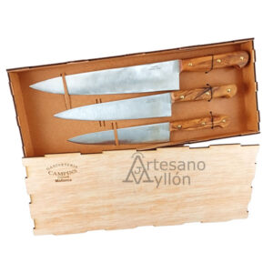 Juego de cuchillos Chef Campins compuesto por tres cuchillos de cocina con hojas de acero inoxidable y mangos de madera de olivo, presentados en una caja de madera con interior acolchado sobre fondo claro.